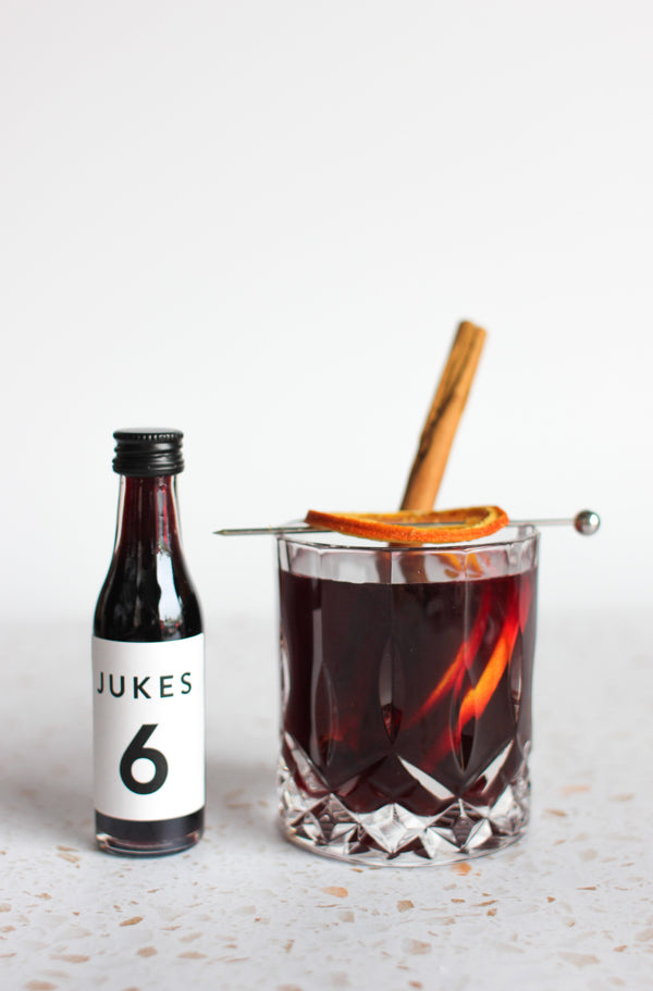 Jukes 6 concentrate bottle next to a crystal glass of jukes mulled drink with dried oranges and a cinnamon stick 